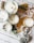 Several candles are arranged on a wooden surface, each in a glass container, with various decorations such as dried flowers, herbs, and pine cones around them. The setup includes autumn leaves and wooden beads, enhancing the rustic and cozy atmosphere.