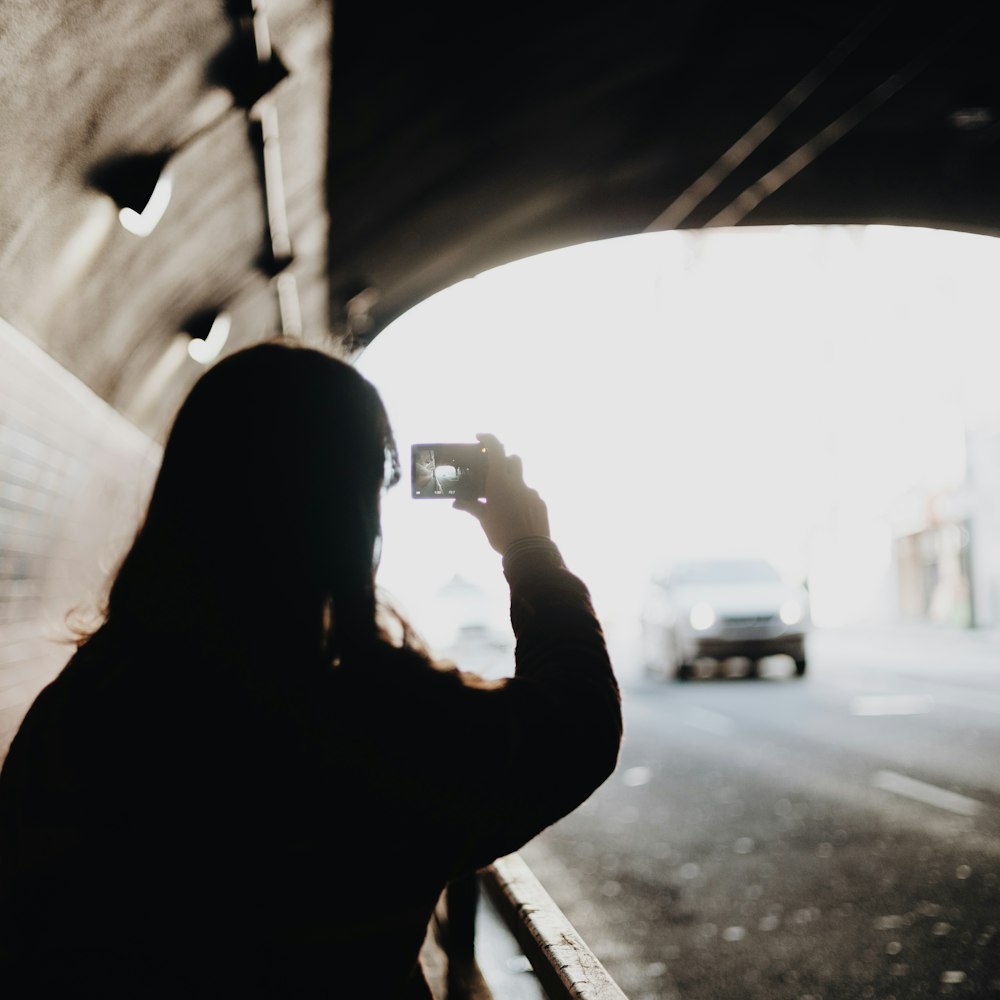 a woman taking a picture of a car through a tunnel