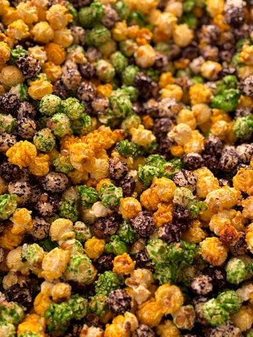 A close-up view of multicolored popcorn, featuring vibrant shades of green, brown, yellow, and white. Each piece is coated with assorted flavors and appears crunchy and appetizing.