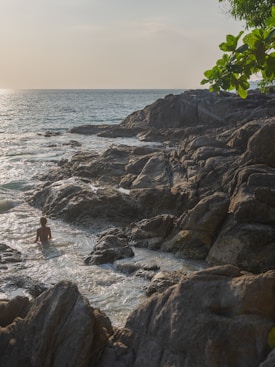 a person wading in a body of water near rocks