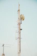A tall communication tower with metal lattice structure and multiple antennas, including a large dish antenna, all set against a clear blue sky.
