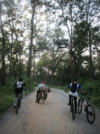 Albert guiding a small group of cyclists along a sunlit forest trail with mountains in the background.