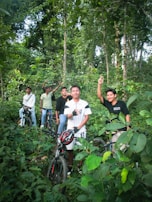 Cyclists sharing laughs and stories during a break on a forest trail surrounded by tall trees.