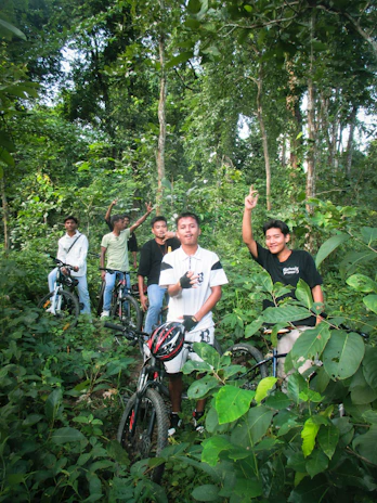 Group of friends laughing and resting beside their bikes near a wooden trail sign.
