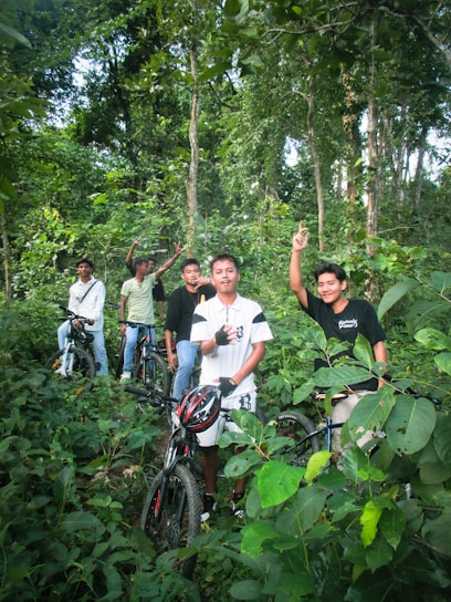 Smiling group of cyclists taking a break on a sunny trail surrounded by lush greenery.