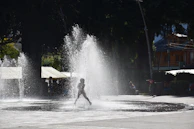 A candid street photo showing a child playing joyfully under a spray of water on a hot day.
