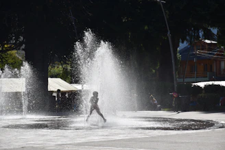 A candid street photo showing a child playing joyfully under a spray of water on a hot day.
