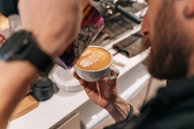 Barista carefully pouring latte art into a creamy coffee cup with lush greenery in the background.