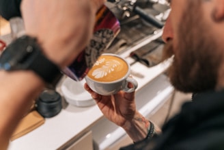 Barista carefully pouring latte art into a creamy coffee cup with lush greenery in the background.