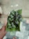 A hand holding a green leafy bunch wrapped in a banana leaf, with a tiled floor visible in the background.