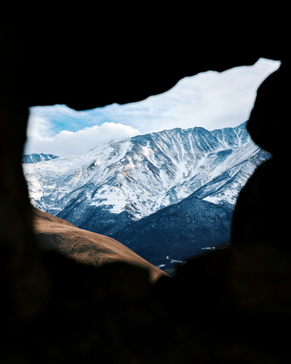 uma vista de uma cordilheira através de um buraco em uma rocha