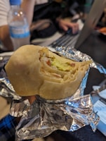 A warm burrito wrapped in foil, with rice and beans spilling out.