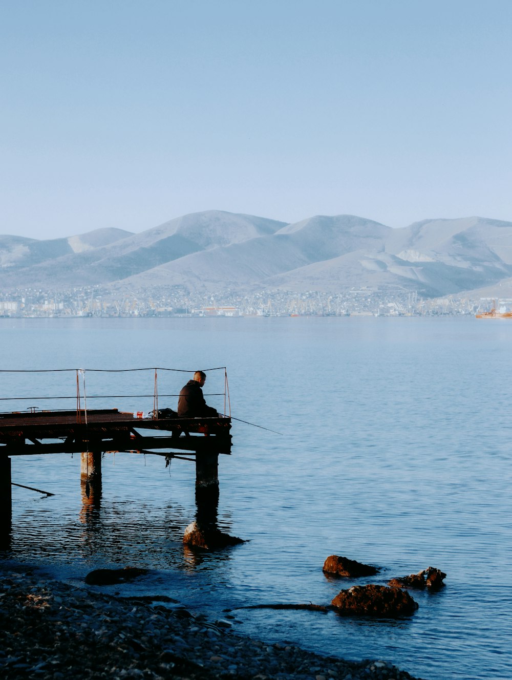 a man is sitting on a dock by the water