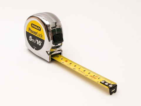 A metal measuring tape with the brand 'Stanley' and 'PowerLock' written on the casing. The tape is extended and shows measurements in both metric and imperial units. The casing is shiny and reflective, primarily silver with black and yellow labeling.
