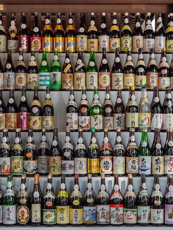 Selection of sake bottles lined up on a rustic wooden shelf, ready to be served.