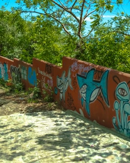 Young artists painting the mural on a sunny day in Cali, surrounded by lush greenery.