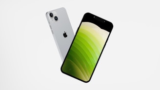 Two smartphones are floating in mid-air against a plain white background. The phones are angled to showcase both their front and back sides. The front side displays a screen with a gradient of green shades, while the back side has a silver finish and a recognizable logo.