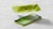 A lime green smartphone is split into two parts, with the back and front panels separated. The back panel features a dual camera system, while the front shows a screen displaying a green abstract pattern. The phone is set against a simple gray background, emphasizing its sleek design.