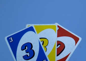 Three playing cards prominently feature the number three in different colors: blue, yellow, and red. These cards are fanned out against a plain background.