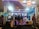 A booth at a trade exhibition with several people gathered around looking at promotional information. The booth features displays and a seating area, surrounded by vibrant advertisements with text about discounts and offers related to water heaters.