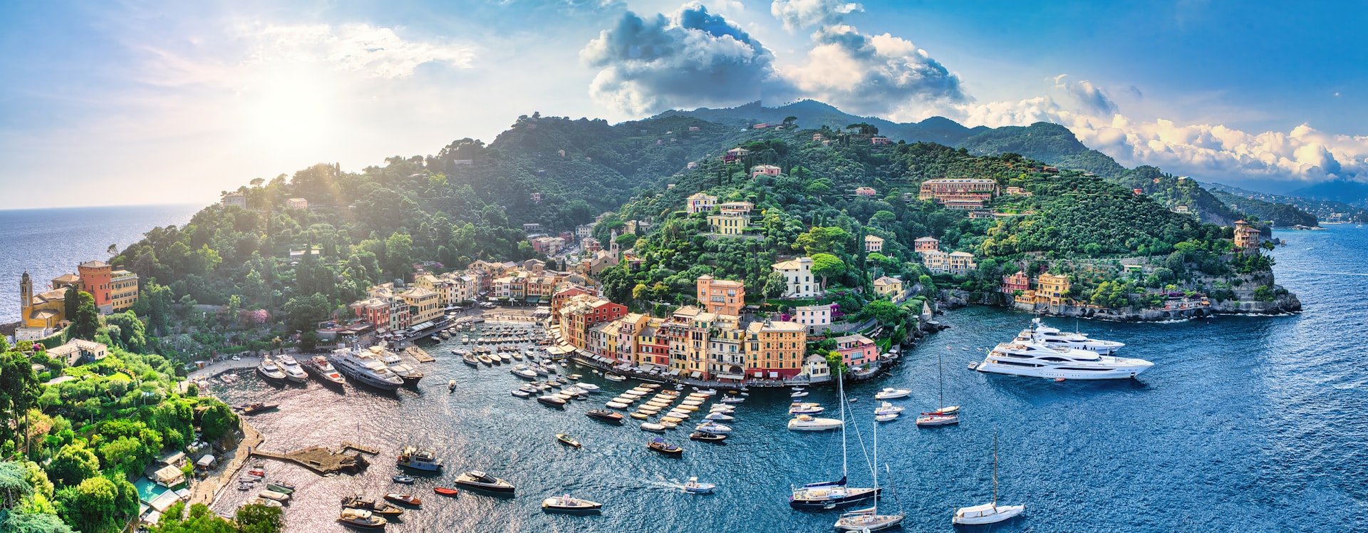 A vibrant island village with colorful houses nestled among lush green hills, with fishing boats bobbing in a sparkling harbor at sunset.
