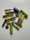 A collection of various batteries of different sizes and colors scattered on a white surface. The batteries include cylindrical AA or AAA types in yellow, green, and blue, as well as flat, coin-shaped ones.