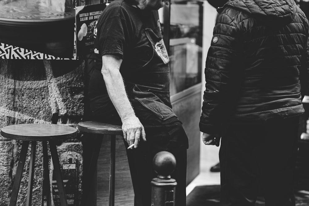 a black and white photo of a man sitting on a stool