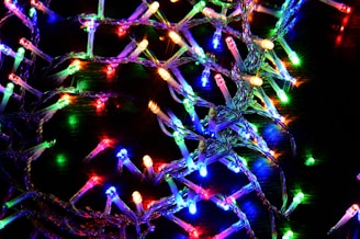 A cluster of colorful LED string lights intertwined and spread across a dark background. The lights display a variety of bright colors including red, blue, green, yellow, and purple, creating a vibrant and festive appearance.