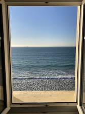 View from the studio window showing a calm beach scene with gentle waves and blue skies.