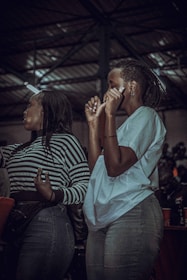 Two people are enjoying themselves in a lively indoor setting, wearing casual clothes. The environment is dimly lit with metal structural elements visible in the background. They appear to be dancing or moving rhythmically, with one person wearing a striped shirt and the other in a plain T-shirt.
