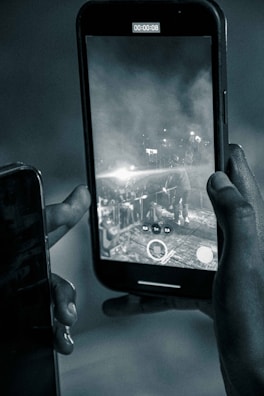 A person is holding a smartphone that is recording a video, as indicated by the on-screen timer showing 00:00:08. The screen displays a scene with another individual at what appears to be a concert or event stage, with bright lights and smoke or fog filling the background.