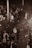A singer on stage is holding a microphone, performing in front of a large crowd. The scene is captured in sepia tones, giving it a classic and nostalgic feel. The backdrop is a blurred audience, indicating movement and energy.