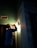 A person wearing a hard hat is inspecting a light fixture on a wall using a flashlight. The setting is dimly lit, suggesting an indoor environment, possibly under maintenance or construction. Shadows cast by the flashlight create a dramatic effect.