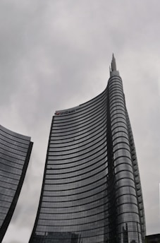 Tall, modern skyscrapers with curved facades rise against a cloudy sky, one bearing the UniCredit logo near its top.