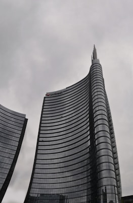 Tall, modern skyscrapers with curved facades rise against a cloudy sky, one bearing the UniCredit logo near its top.