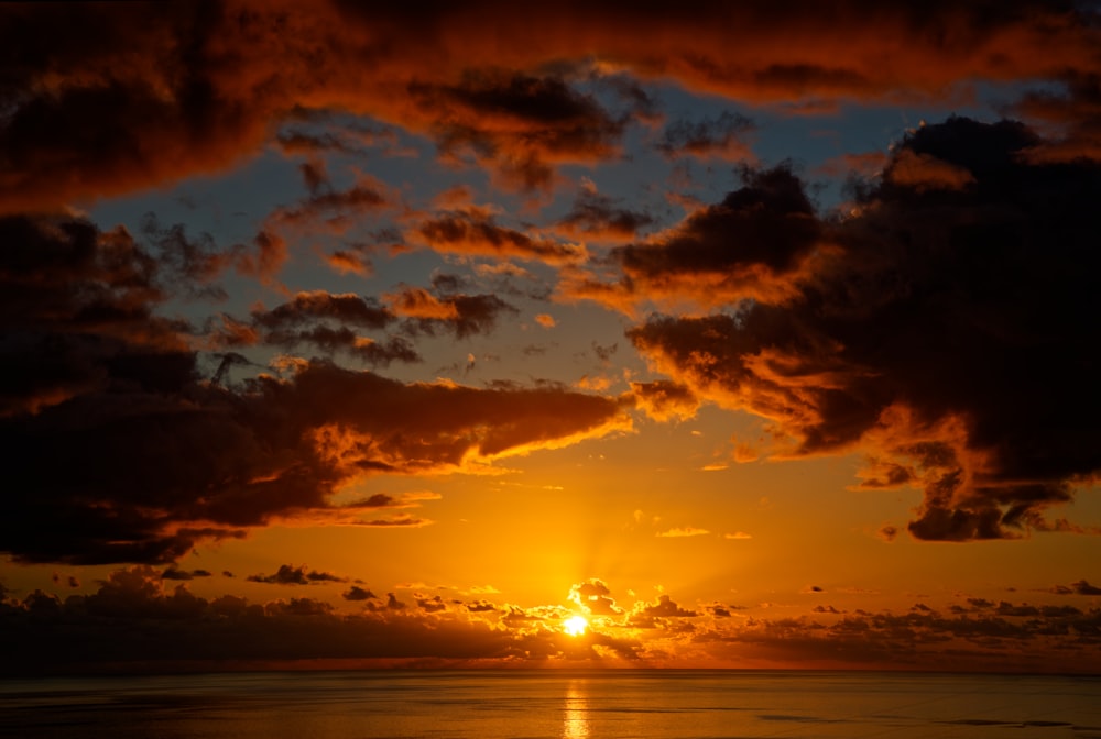 the sun is setting over the ocean on a cloudy day