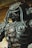 A detailed metallic sculpture resembling a futuristic or robotic warrior. The sculpture features intricate designs with various mechanical components, chains, and tube-like protrusions. Its overall appearance is rugged and complex, reflecting a high level of craftsmanship.