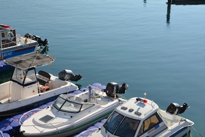 Several small boats are docked at a calm marina, tied to floating blue platforms with visible outboard motors.