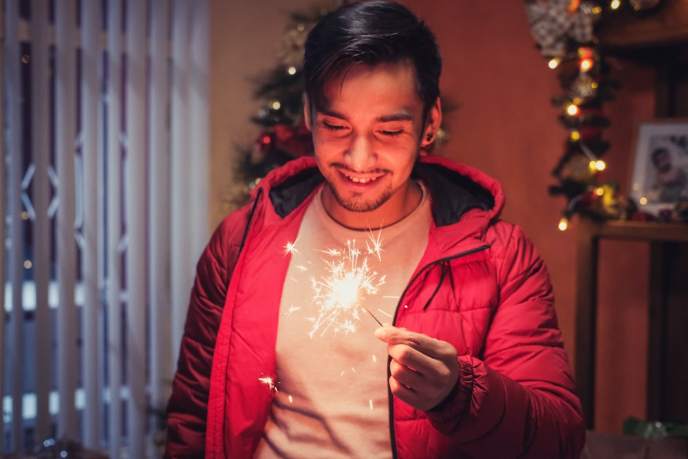 Un hombre sosteniendo una bengala frente a un árbol de Navidad