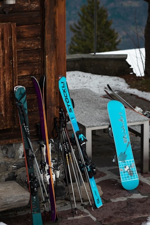Close-up of colorful ski boots and poles resting in the snow beside a cozy mountain cabin.
