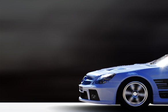 A sleek blue car is positioned on the right side against a dark, blurred background, emphasizing its aerodynamic design and metallic finish. The car features prominent wheel rims and a detailed front grille.