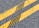 Two parallel yellow lines on an asphalt road with cracks and leaves scattered on the surface.