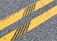 Two parallel yellow lines on an asphalt road with cracks and leaves scattered on the surface.