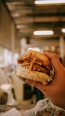 Hands holding a loaded burger with fresh ingredients against a warm, blurred background.