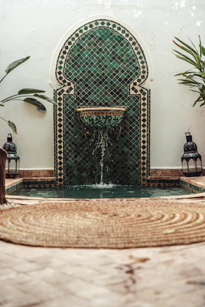 A vibrant Moroccan mosaic fountain surrounded by lush greenery in the riad garden.