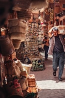 A bustling marketplace filled with an array of vibrant items. Multiple woven baskets are displayed on the left, while in the center, a variety of hanging artifacts, heart-shaped decorations, and small trinkets are visible.