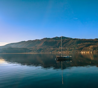 A serene lakeside view in Ireland with lush green hills and a small boat floating on calm water.