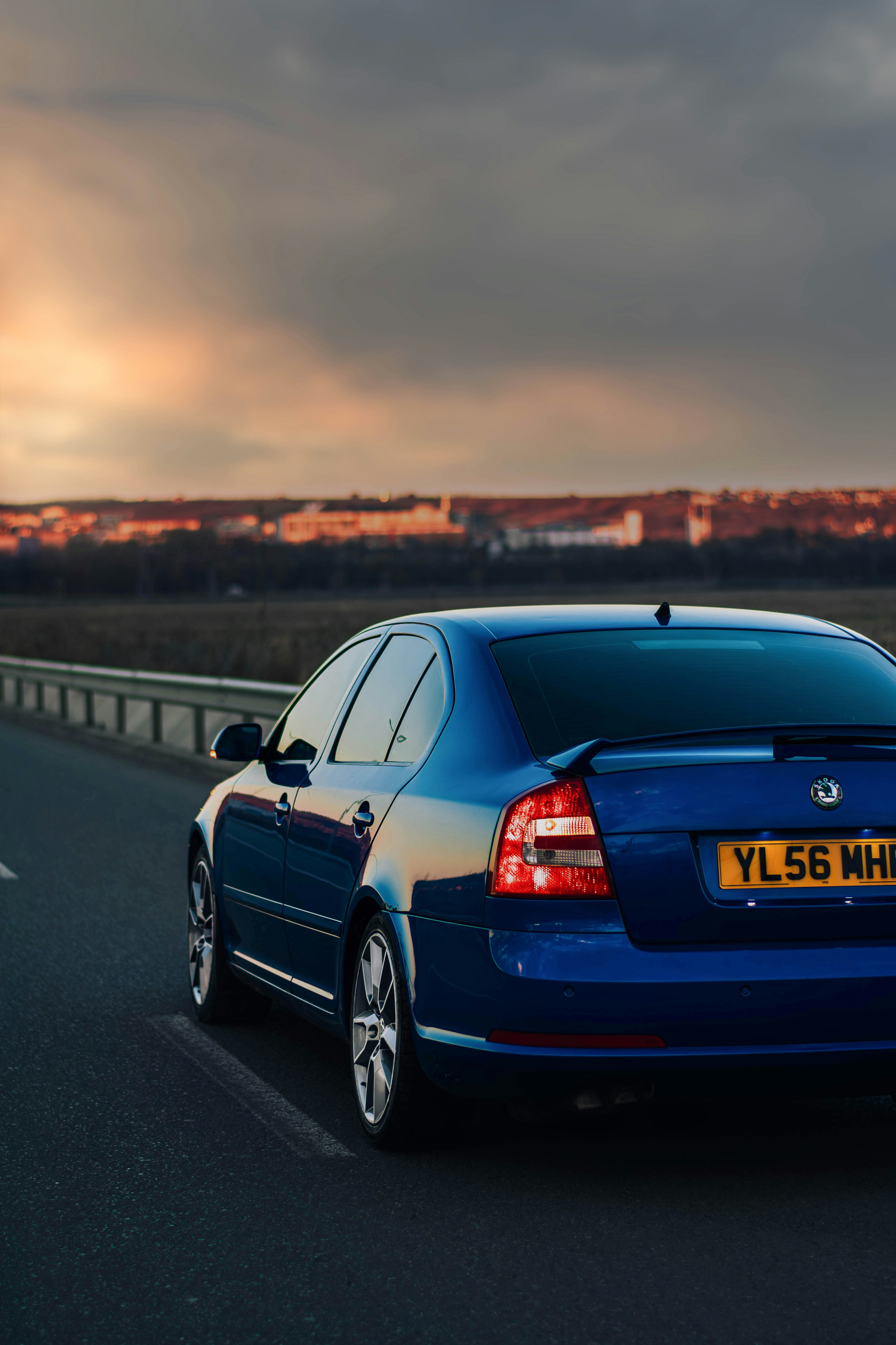a blue car driving down a highway under a cloudy sky