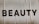 Large, bold letters spelling the word 'BEAUTY' are displayed on a textured surface. The background appears to have a subtle beige tint with visible creases or folds.