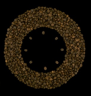 A circular arrangement of coffee beans on a black background, forming a ring with additional beans placed in the center, resembling the face of a clock.